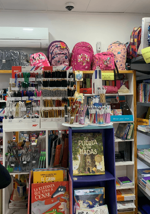 Estantes de papelería con mochilas coloridas, gran variedad de bolígrafos, lápices y libros infantiles.