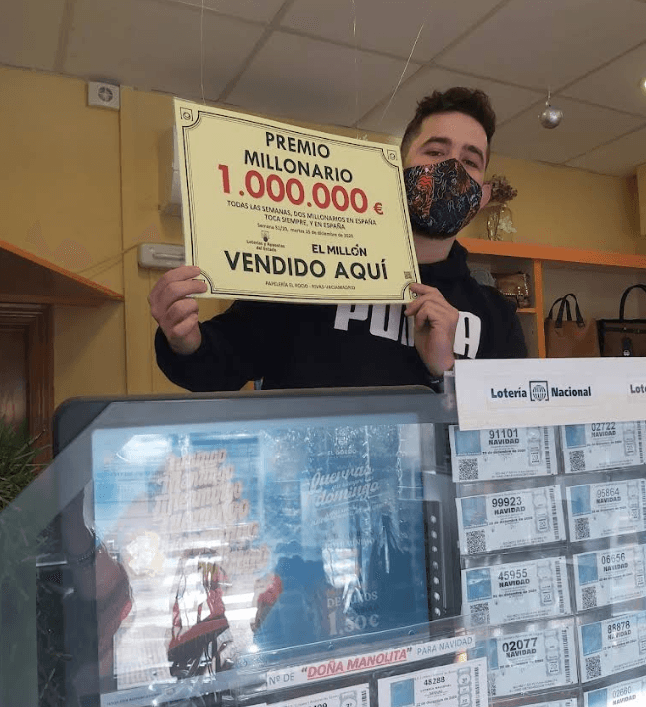 Hombre con mascarilla sostiene cartel de premio de un millón de euros en una administración.