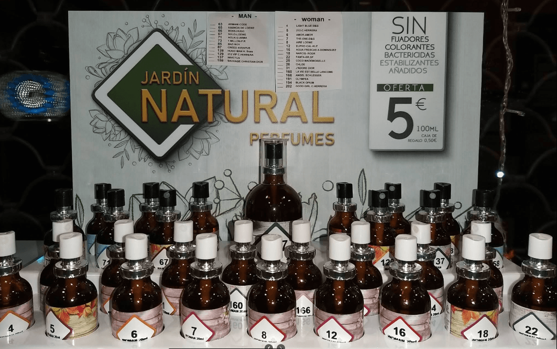 Exhibición de perfumes Jardín Natural con frascos de vidrio ámbar numerados y cartel de precios.